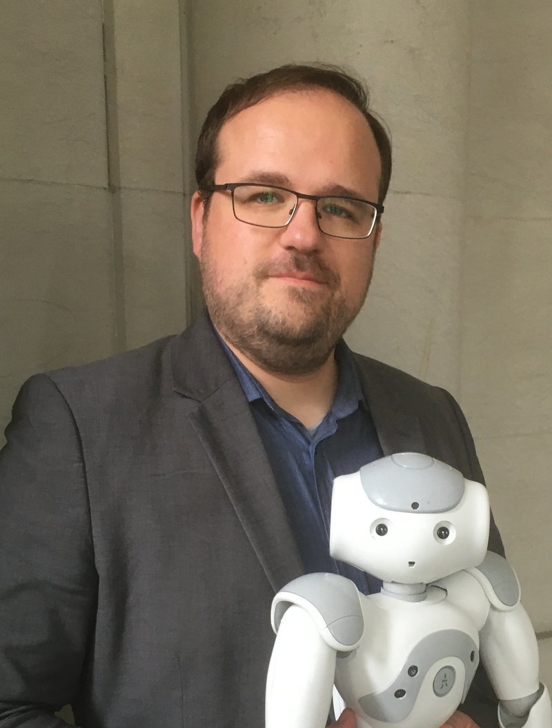 Freundlicher Mann im Anzug mit einem kleinen humanoiden Roboter in den Händen.