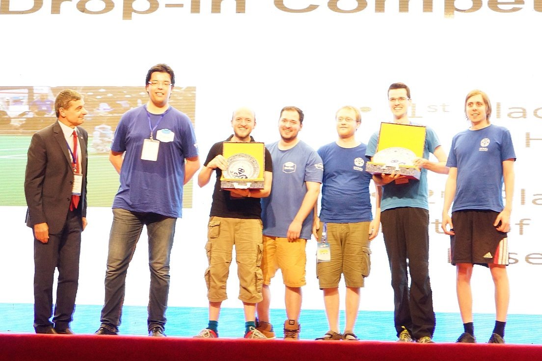 Gruppenfoto einen 6-köpfigen Teams lächelnd auf einer Bühne, neben ihnen ein Mann im Anzug.